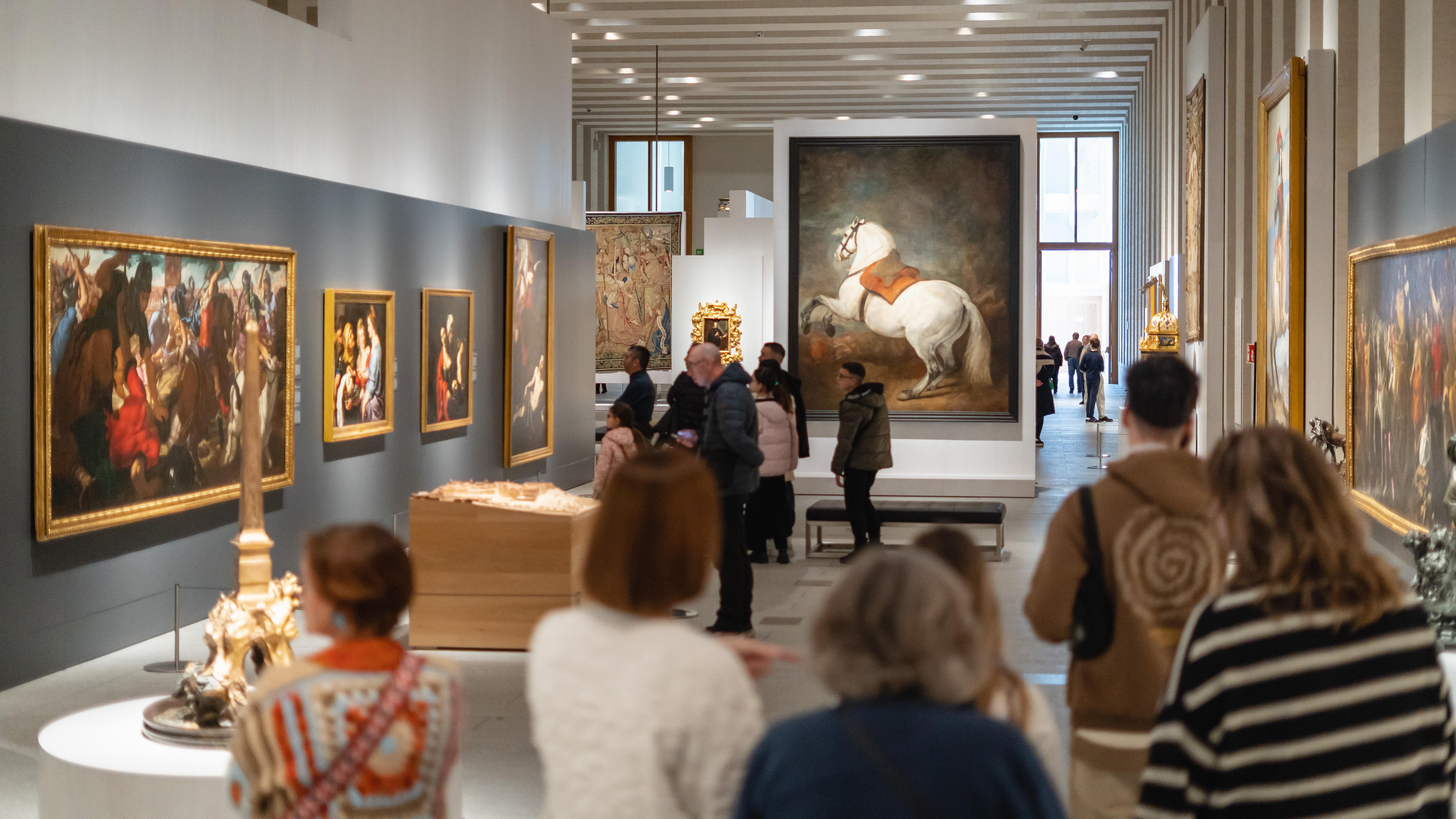 interior de sala de exposiciones con grandes cuadros y gente de espaldas