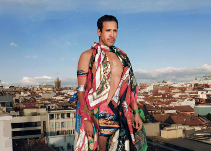 Hombre en una azotea, vestido con pañuelos estampados de diferentes colores. Al fondo se ven tejados de edificios.