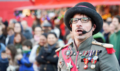 hombre con bombín y chaqueta militar con muchas condecoraciones en el pecho, micrófono en la boca, público de fondo