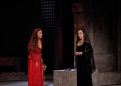 dos mujeres sobre un escenario, mujer con vestido rojo y cara de sorpresa, mujer de negro con peineta y mantilla con cara dramática, colgante con forma de cruz al cuello